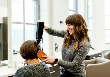 Peluquera trabajando el cabello de una clienta frente al espejo